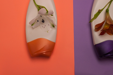 Flowers and beauty, decorative cosmetics bottles. Peach and purple colors background, flat lay, top view, minimalism.の写真素材