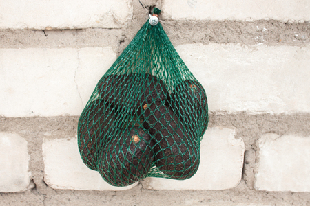 Fresh organic hass avocados in a green string bag on a white background isolated, healthy food concept, copy space.の写真素材