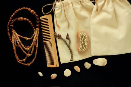 Zero waste women's accessories, natural body brush, wooden hair comb and beads, reusable cotton hand made shopping bags. Tree branch, natural smooth sea stones, black background, copy space,flat lay.の写真素材