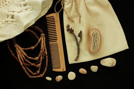Zero waste women's accessories, natural body brush, wooden hair comb and beads, straw hat, reusable cotton hand made bag. Tree branch, natural smooth sea stones, black background, copy space,flat lay.の写真素材