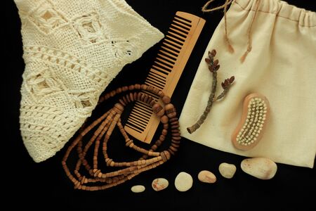 Zero waste women's accessories, natural body brush, wooden hair comb and beads, straw hat, reusable cotton hand made bag. Tree branch, natural smooth sea stones, black background, copy space,flat lay.の写真素材