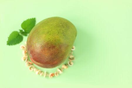 Ripe Green and Red Mango with green leaves and seashells beads on mint pastel background. Bright colors, Tropical Fruits, summer vacation,vegan.Poster,banner,streamer.Copy space,minimalistic style.の写真素材