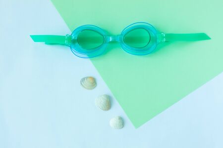 Summer flatlay with watersport goggles and seashells, mint and light blue background, minimalistic style, copy space. Sea rest, vacation with family, children's goggles.の写真素材