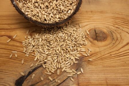 Raw oat grains in a coconut shell, low-calorie ingredient for delicious healthy breakfast on a wooden background, copy space. Nutritious whole grains, wholesome goodness and great tasting variety.の写真素材