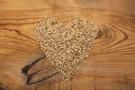 Heartshaped raw oat grains, low-calorie ingredient for delicious healthy breakfast on a wooden background, copy space. Nutritious whole grains, wholesome goodness and great tasting variety.の写真素材