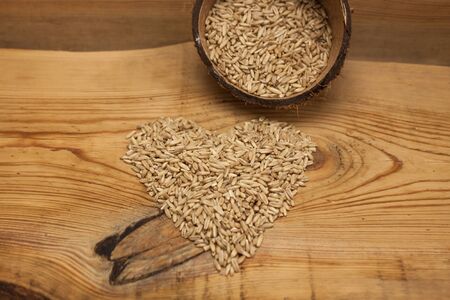 Heartshaped raw oat grains in a coconut shell, ingredient for delicious healthy breakfast on a wooden background, copy space. Nutritious whole grains, wholesome goodness and great tasting variety.の写真素材
