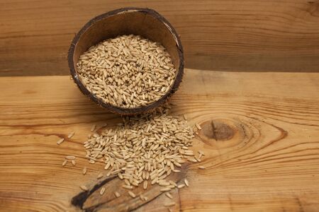 Raw oat grains in a coconut shell, low-calorie ingredient for delicious healthy breakfast on a wooden background, copy space. Nutritious whole grains, wholesome goodness and great tasting variety.の写真素材