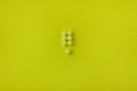 Pills in a shape of exclamation mark on a yellow background. Flat lay, top view, minimalistic style....