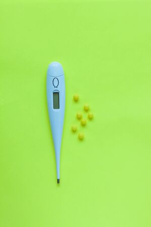 Pills and white digital thermometer on a yellow background. Flat lay, top view, minimalistic style. Vitamins, drugs, dietary supplements, cure disease.の写真素材