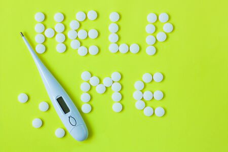 White pills in a shape of a words Help Me with a digital thermometer on a yellow background. Flat lay, top view, minimalistic style. Vitamins, treatments, drugs, dietary supplements.の写真素材