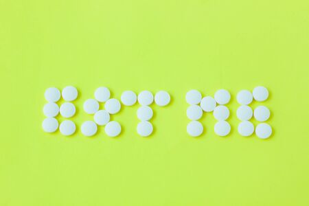 White pills in a shape of a words Eat Me on a yellow background. Flat lay, top view, minimalistic style. Vitamins, drugs, dietary supplements.の写真素材