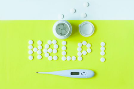 White pills in a shape of a word Help with a digital thermometer and a can of drugs on a yellow background. Flat lay, top view, minimalistic style. Vitamins, treatments, dietary supplements.の写真素材