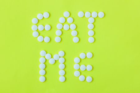 White pills in a shape of a words Eat Me on a yellow background. Flat lay, top view, minimalistic style. Vitamins, drugs, dietary supplements.の写真素材