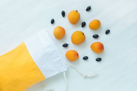 Cotton shopping bag with organic eco apricot fruits on white linen background.Caring for the environment, low plastic concept, zero waste,mindful eating. Yellow and white fabric hand made bag top viewの写真素材