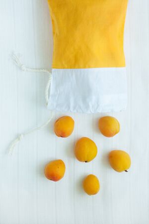 Cotton shopping bag with organic eco apricot fruits on white linen background.Caring for the environment, low plastic concept, zero waste,mindful eating. Yellow and white fabric hand made bag top viewの写真素材