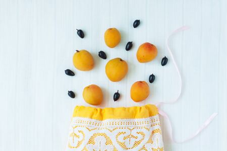 Cotton shopping bag with organic eco apricot fruits on white linen background.Caring for the environment, low plastic concept, zero waste,mindful eating. Yellow fabric hand made bag with lace,top viewの写真素材