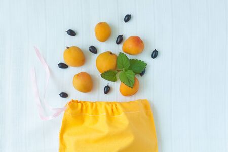 Cotton shopping bag with apricot fruits and mint leaves on white linen background.Caring for the environment,low plastic concept,zero waste,mindful eating.Yellow and white fabric hand made bag,flatlayの写真素材