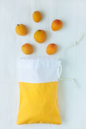 Cotton shopping bag with organic eco apricot fruits on white linen background.Caring for the environment, low plastic concept, zero waste,mindful eating. Yellow and white fabric hand made bag top viewの写真素材