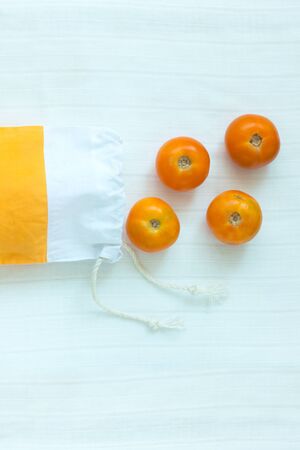 Cotton shopping bag with organic eco yellow tomatoes on white linen background.Caring for the environment, low plastic concept, zero waste,mindful eating. Yellow and white fabric hand made bag,flatlayの写真素材