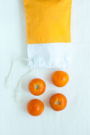 Cotton shopping bag with organic eco yellow tomatoes on white linen background.Caring for the environment, low plastic concept, zero waste,mindful eating. Yellow and white fabric hand made bag,flatlayの写真素材