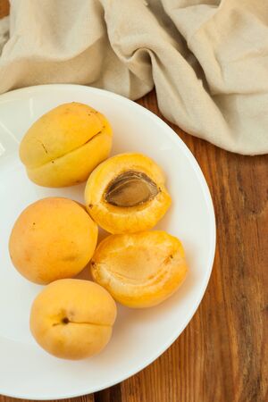 Ripe fresh apricot fruits on a white plate on the wooden background, linen towel, tablecloth. Copy space, delisious healthy food, vegan, raw. Minimalistic style.の写真素材