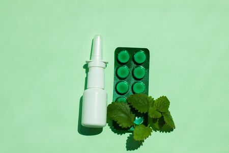 White medical nasal spray bottle and green tablets plate, a remedy against allergies and runny nose, colds, viral diseases. Mint leaves, green background, flat lay, natural light, minimalistic style.の写真素材