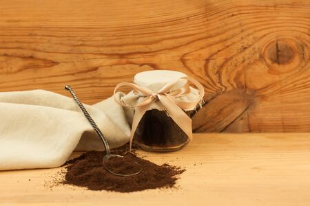 A glass jar of ground coffee with linen fabric and ribbon, an antique spoon. Body scrub, mixed sugar, oil and essentials. Homemade cosmetic for peeling and spa care. Wooden background, copy space.の写真素材