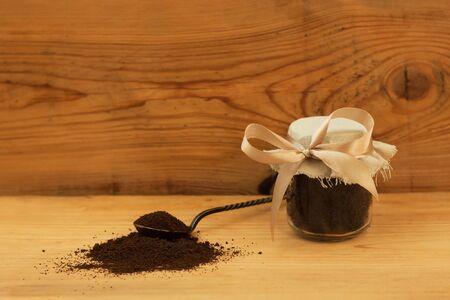 A glass jar of ground coffee with linen fabric and ribbon, an antique spoon. Body scrub, mixed sugar, oil and essentials. Homemade cosmetic for peeling and spa care. Wooden background, copy space.の写真素材