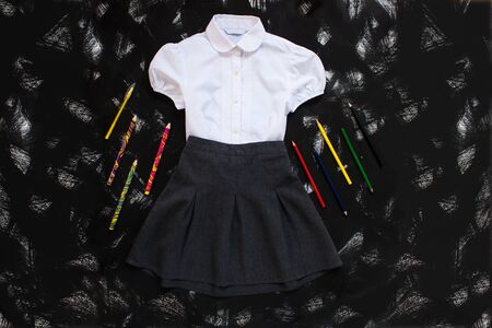 White shirt, grey skirt and stationery on black background. Uniform. The first of september, new school year supplies. Back to school banner, education concept. Top view, flatlay, copy space.の写真素材