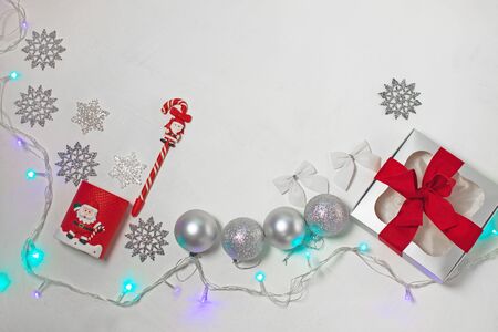 Christmas composition of red and silver decorations, gift box with ribbon bow, balls and snowflakes on a white background with lights, flatlay. New year, winter, holidays concept.Top view, copy space.の写真素材