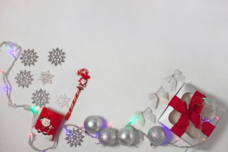 Christmas composition of red and silver decorations, gift box with ribbon bow, balls and snowflakes on a white background with lights, flatlay. New year, winter, holidays concept.Top view, copy space.の写真素材