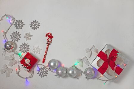 Christmas composition of red and silver decorations, gift box with ribbon bow, balls and snowflakes on a white background with lights, flatlay. New year, winter, holidays concept.Top view, copy space.の写真素材