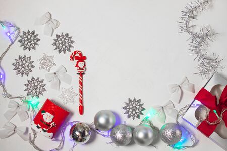 Christmas composition of red and silver decorations, gift box with ribbon bow, balls and snowflakes on a white background with lights, flatlay. New year, winter, holidays concept.Top view, copy space.の写真素材