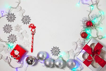 Christmas composition of red and silver decorations, gift box with ribbon bow, balls and snowflakes on a white background with lights, flatlay. New year, winter, holidays concept.Top view, copy space.の写真素材