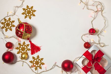 Christmas present box with red ribbon, gold decorations, balls, snowflakes and lights on a white background. New year concept, holidays composition, winter flatlay. Top view. Copy space.の写真素材