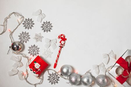 Christmas composition of red and silver decorations, gift box with ribbon bow, balls and snowflakes on a white background with lights, flatlay. New year, winter, holidays concept.Top view, copy space.の写真素材