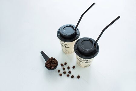 Kraft paper coffee cup with black lid and tubule from street shop with a spoon of coffee beans on light background. Lifestyle concept, take away drinks. Copy space, front view.の写真素材