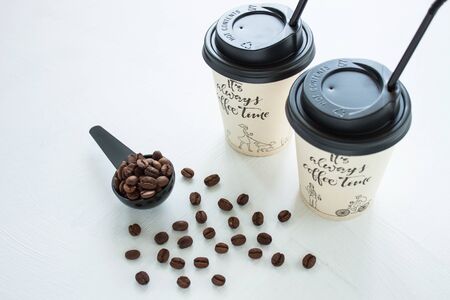 Kraft paper coffee cup with black lid and tubule from street shop with a spoon of coffee beans on light background. Lifestyle concept, take away drinks. Copy space, front view.の写真素材