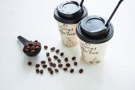 Kraft paper coffee cup with black lid and tubule from street shop with a spoon of coffee beans on light background. Dark chocolate candies,sweets.Lifestyle concept,take away drinks.Copy space,top viewの写真素材