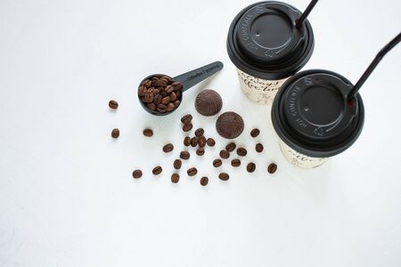 Kraft paper coffee cup with black lid and tubule from street shop with a spoon of coffee beans on light background. Dark chocolate candies,sweets.Lifestyle concept,take away drinks.Copy space,top viewの写真素材