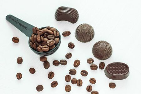 Dark chocolate candies, sweets with a spoon of coffee beans on light background. Measuring spoon for tea and coffee serving.Copy space, top view.の写真素材