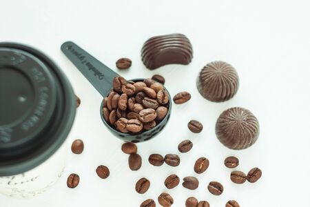 Dark chocolate candies,sweets with a spoon of coffee beans on light background. Lifestyle concept,kraft paper coffee cups with black lid, take away drinks. Copy space,top view.の写真素材