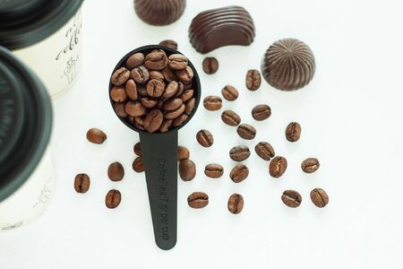 Dark chocolate candies,sweets with a spoon of coffee beans on light background. Lifestyle concept,kraft paper coffee cups with black lid, take away drinks. Copy space,top view.の写真素材
