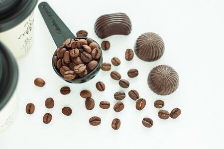 Dark chocolate candies,sweets with a spoon of coffee beans on light background. Lifestyle concept,kraft paper coffee cups with black lid, take away drinks. Copy space,top view.の写真素材