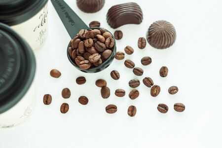 Dark chocolate candies,sweets with a spoon of coffee beans on light background. Lifestyle concept,kraft paper coffee cups with black lid, take away drinks. Copy space,top view.の写真素材