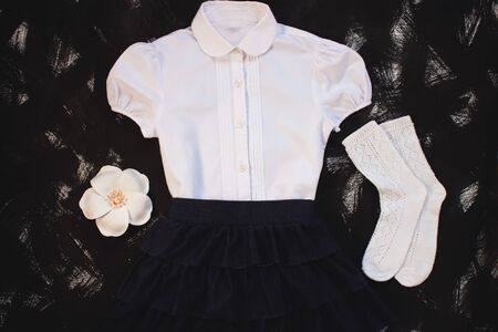 School uniform with white shirt, socks and dark denim skirt on a black background. Fashionable student set for girls, flower hair accessory, back to school concept. Flatlay, top view, copy space.の写真素材