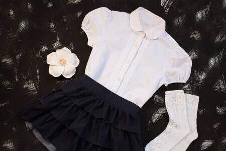 School uniform with white shirt, socks and dark denim skirt on a black background. Fashionable student set for girls, flower hair accessory, back to school concept. Flatlay, top view, copy space.の写真素材