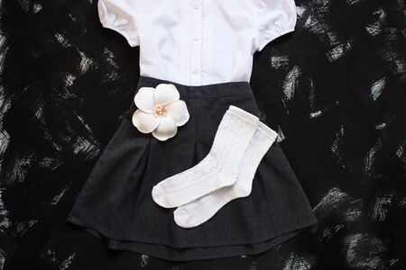 School uniform with white shirt, socks and dark denim skirt on a black background. Fashionable student set for girls, flower hair accessory, back to school concept. Flatlay, top view, copy space.の写真素材