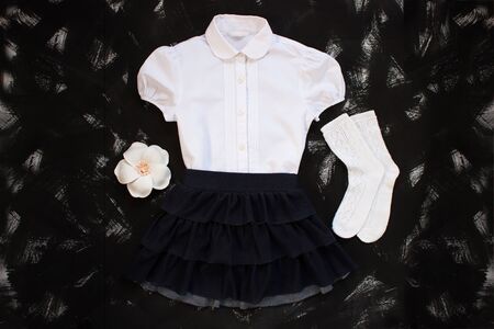 School uniform with white shirt, socks and dark denim skirt on a black background. Fashionable student set for girls, flower hair accessory, back to school concept. Flatlay, top view, copy space.の写真素材