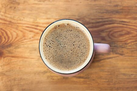 A cup of coffee on brown wooden background. Beautiful foam, pink ceramic mug, stylish toning, top view, flatlay, place for text.の写真素材